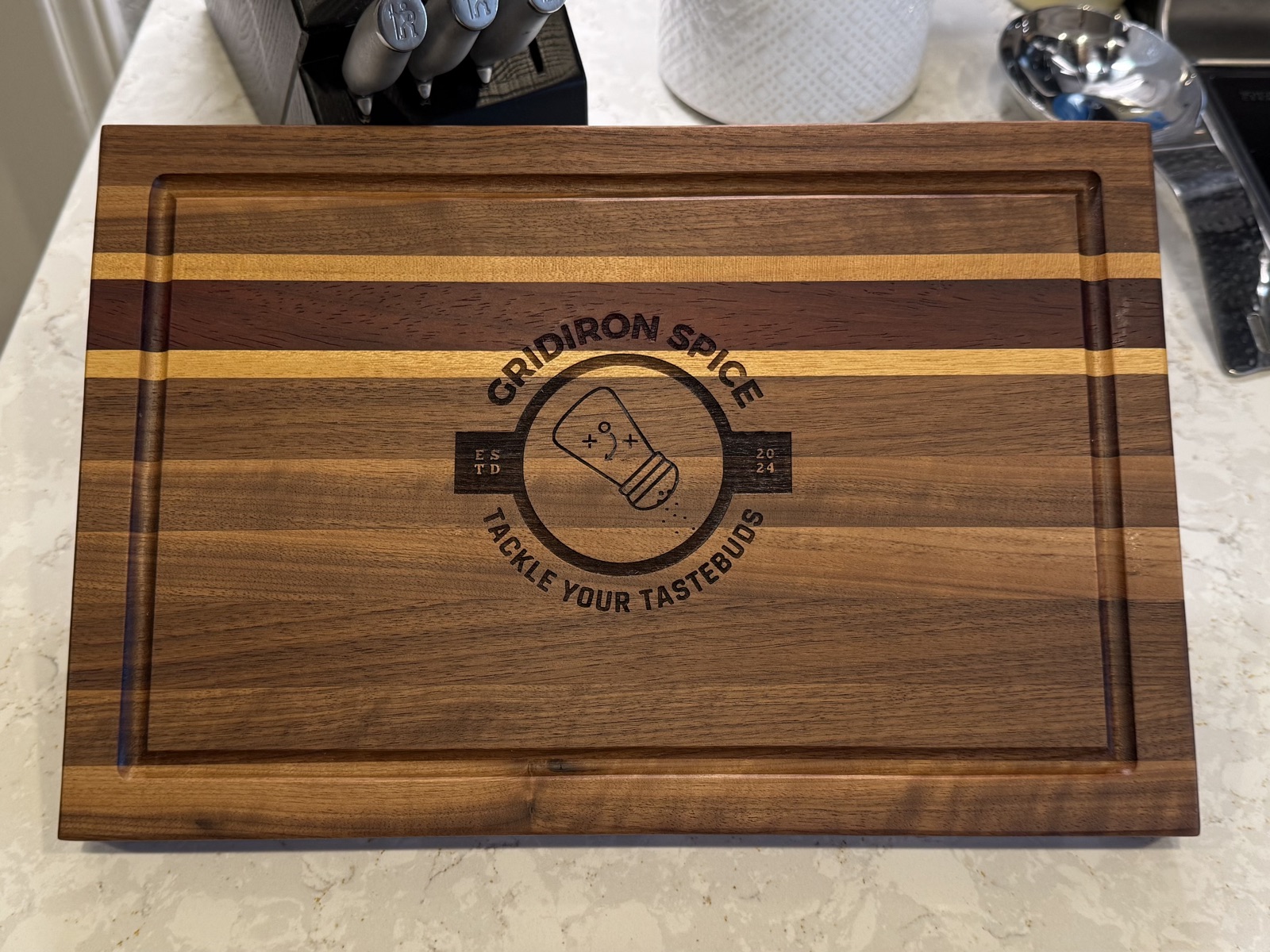 Custom laser-engraved walnut and maple cutting board with Gridiron Spice business logo